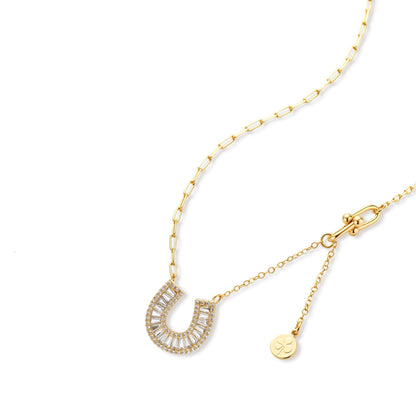 Gold-plated horseshoe necklace and earring set with baguette and round crystals arranged in geometric pattern on white background.
