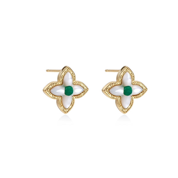 Gold quatrefoil stud earrings with white mother-of-pearl petals and emerald green gemstone center on beige background.