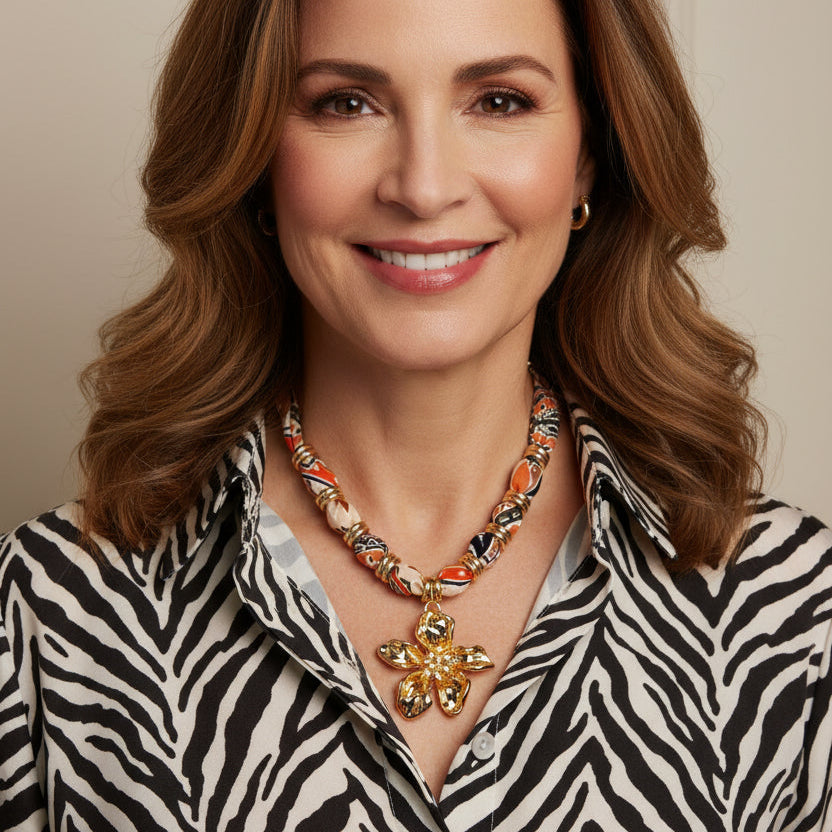 Vibrant patterned fabric necklace with gold-toned flower pendant featuring rhinestone center on white background