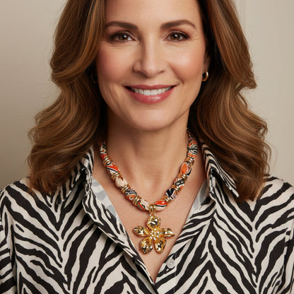 Vibrant patterned fabric necklace with gold-toned flower pendant featuring rhinestone center on white background