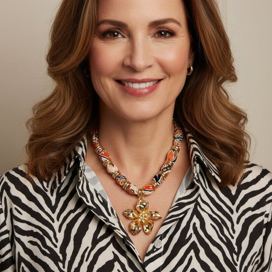 Vibrant patterned fabric necklace with gold-toned flower pendant featuring rhinestone center on white background