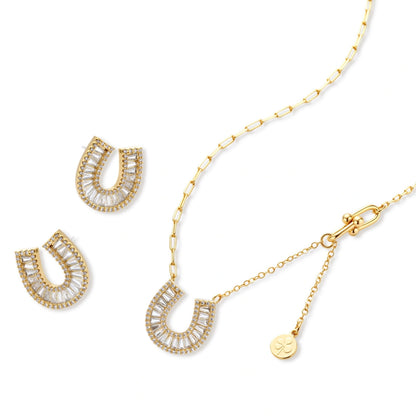 Gold-plated horseshoe necklace and earring set with baguette and round crystals arranged in geometric pattern on white background.