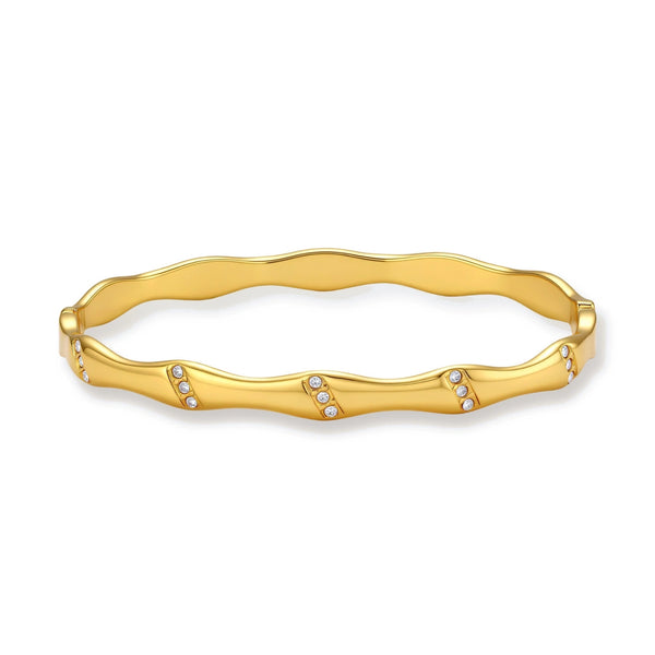 Gold-toned wavy bangle with bamboo-style segments and CZ crystal clusters on cream background. 18K plated stainless steel.