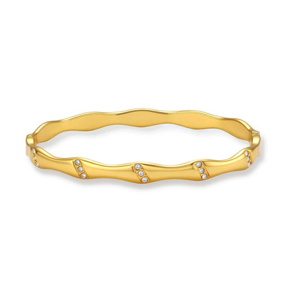 Gold-toned wavy bangle with bamboo-style segments and CZ crystal clusters on cream background. 18K plated stainless steel.